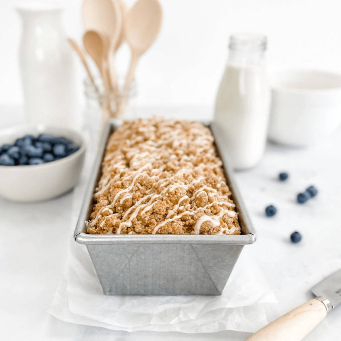 Nonstick aluminized steel loaf pan with freshly baked crumb-topped bread, surrounded by milk, blueberries, and wooden utensils, featured in Kitchen & Food and Baking Supplies collections.