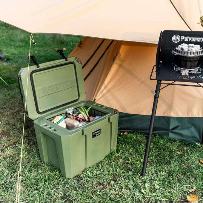 Olive green cooler box with insulated interior open and filled with food, placed on grass near a tan camping tent and portable stove, ideal for Farm, Garden & Tool, Camping, and Best Sellers collections.