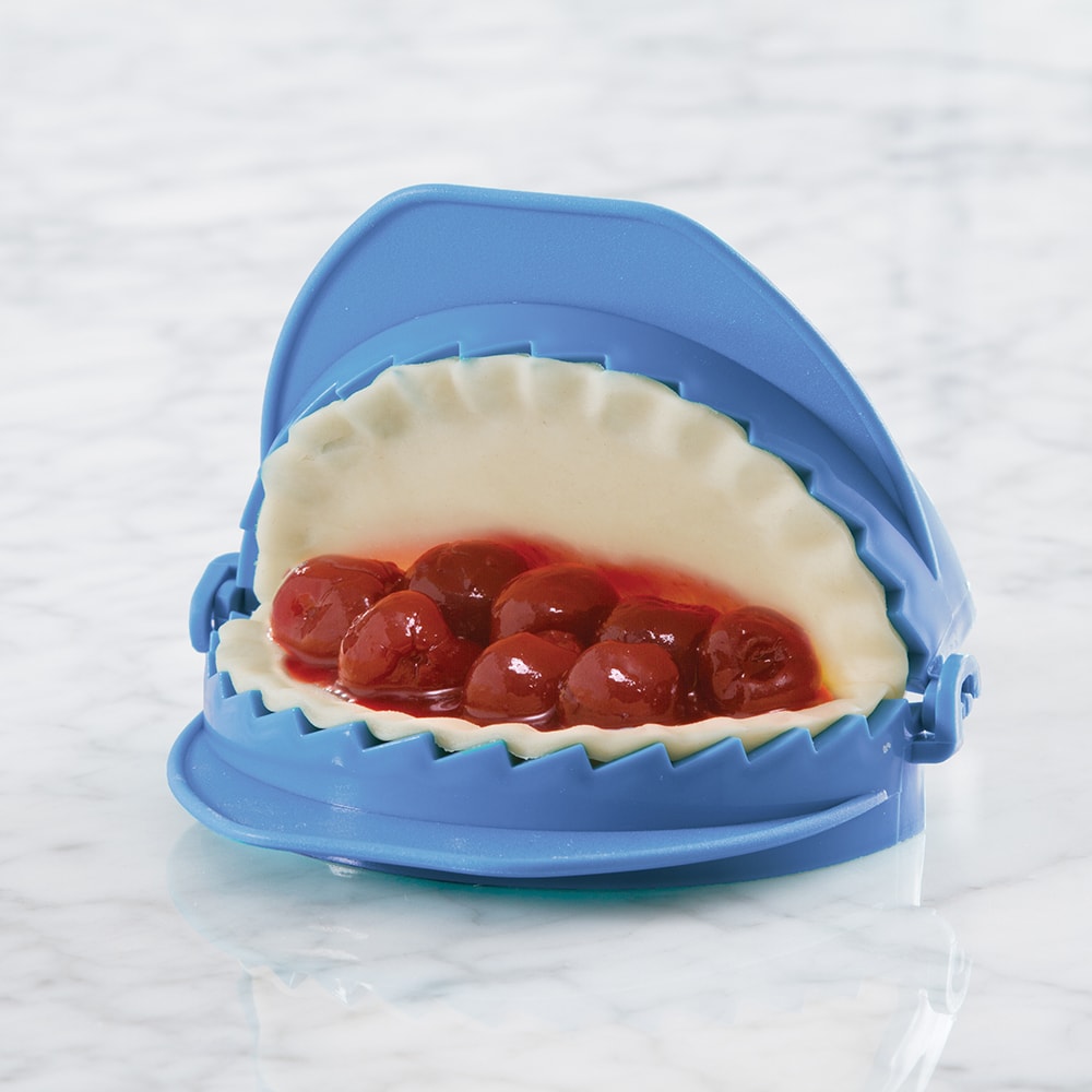 Blue dough press with scalloped edges holding filled cherry hand pie dough, designed for easy shaping and sealing in Kitchen & Food and Baking Helpers collections.