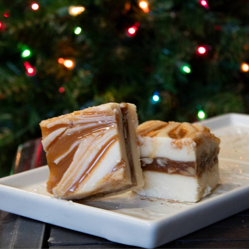 Two bite-sized, creamy fudge pieces with swirls of caramel and chocolate on a white plate, showcasing handcrafted Amish-made quality, ideal for Kitchen & Food and Snacks and Sweets collections.