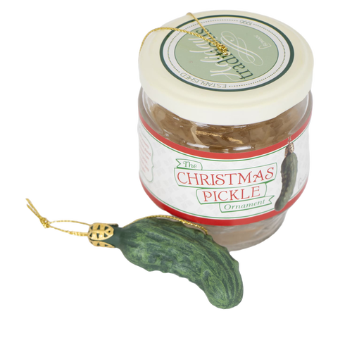 Glass jar containing a festive green pickle-shaped ornament with a gold hanging string, designed for holiday decor and celebrated as a fun seasonal tradition in home collections.