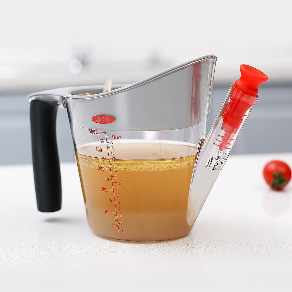 Transparent fat separator featuring a black cushioned grip handle, red stopper, and red measurement markings, designed for Kitchen & Food, Kitchen Gadgets, and Cooking and Baking Helpers collections.