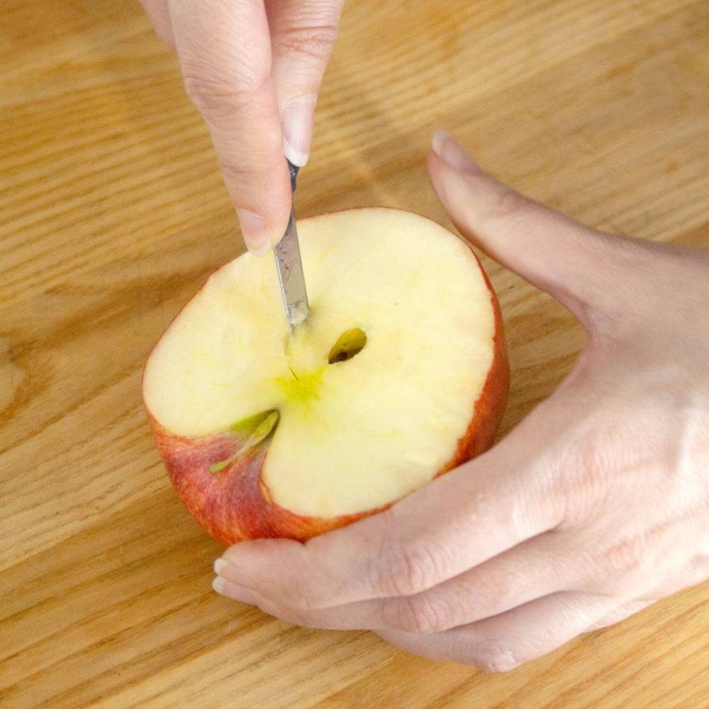 Handcrafted flexible paring knife with a sharp blade gently coring the center of a sliced apple, shown in use on a wooden surface, part of kitchen and food prep collections.