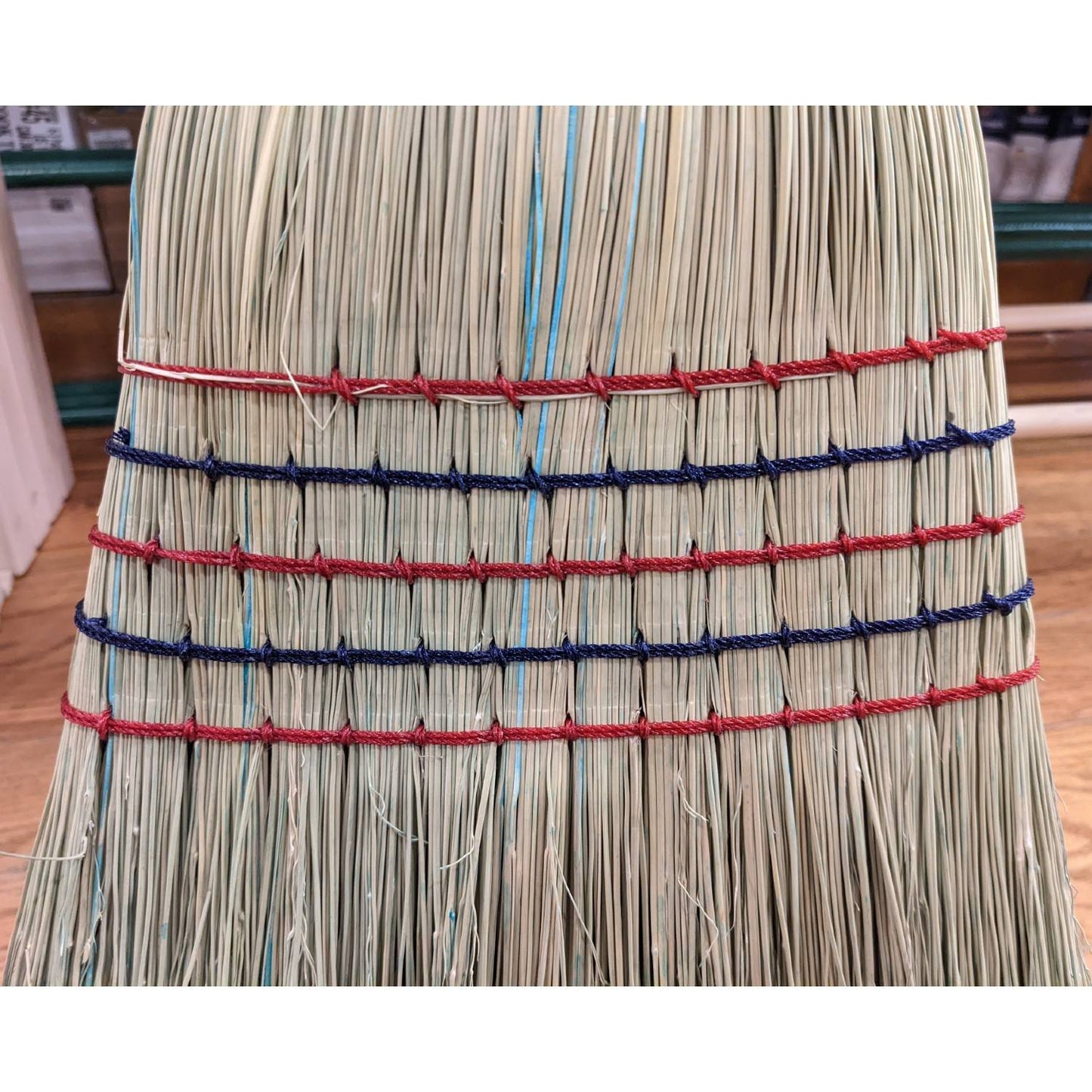 Close-up of a handcrafted large corn broom with tightly bound natural corn straw bristles featuring red and blue stitching, Amish made in the USA for farm, garden, and household cleaning.