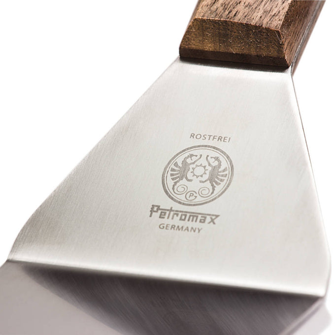 Close-up of a flexible spatula blade made of polished stainless steel with a subtle engraved logo and a smooth walnut handle, designed for grilling and cooking in Kitchen & Food and Cooking Helpers collections.