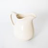 Cream-colored stoneware pitcher with a curved handle and rounded spout, handcrafted in the USA, ideal for serving in Kitchen & Food, Dinnerware, and Storage collections.