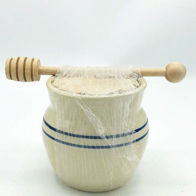 Handcrafted stoneware honey pot in rustic stone color with two classic blue stripes, covered with plastic wrap and topped with a wooden honey dipper, ideal for Kitchen & Food and Storage collections.