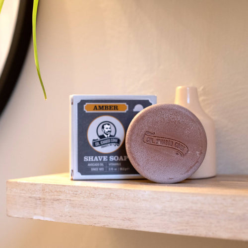 Handcrafted amber shaving soap bar with embossed logo next to its vintage-style box, containing avocado oil, vitamin E, and shea butter, part of USA Made, Health & Wellness, and Grooming collections.