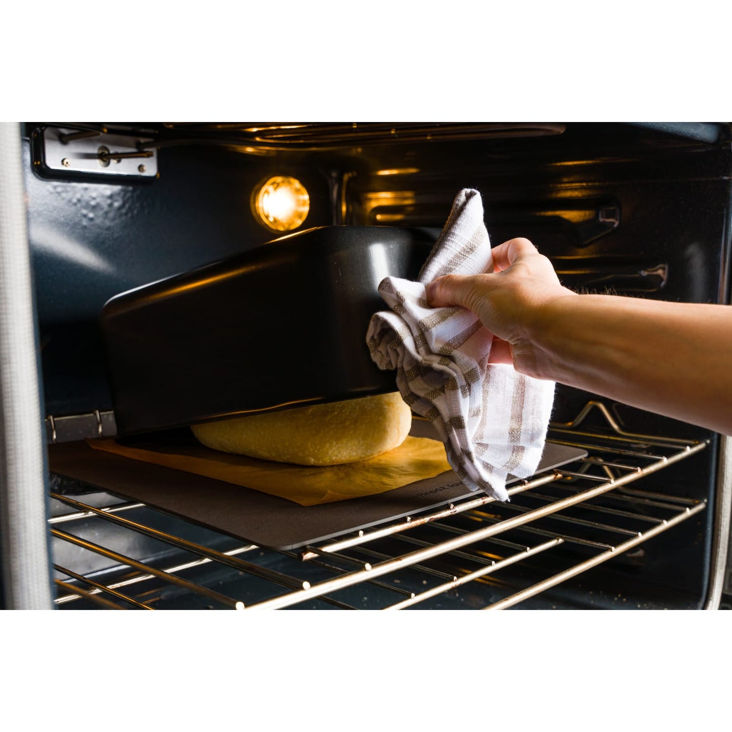 Black Batard baking shell being placed over dough on parchment paper inside a home oven, featured in Kitchen & Food, Cookware, Baking Supplies, and Bread Making Supplies collections.