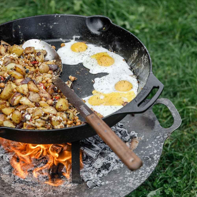 Handcrafted cast iron skillet with two side handles cooking sunny-side-up eggs and seasoned potatoes over an open fire, perfect for farm, camping, kitchen, and cast iron cookware collections.