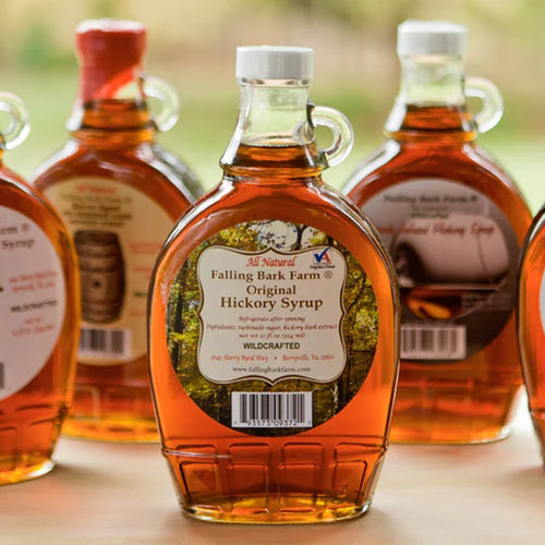 Clear glass bottle filled with amber hickory syrup featuring a white cap and loop handle, labeled as wildcrafted and handmade, displayed on a wooden surface, ideal for Kitchen & Food and USA Made collections.