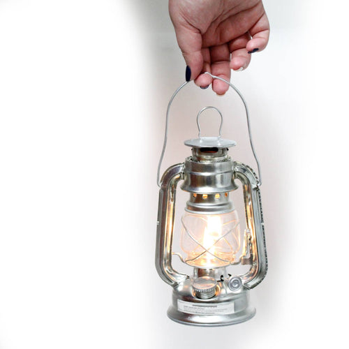 Hand holding a compact galvanized metal lantern with a bright flame, designed for reliable outdoor lighting in camping, emergency supplies, and garden collections.