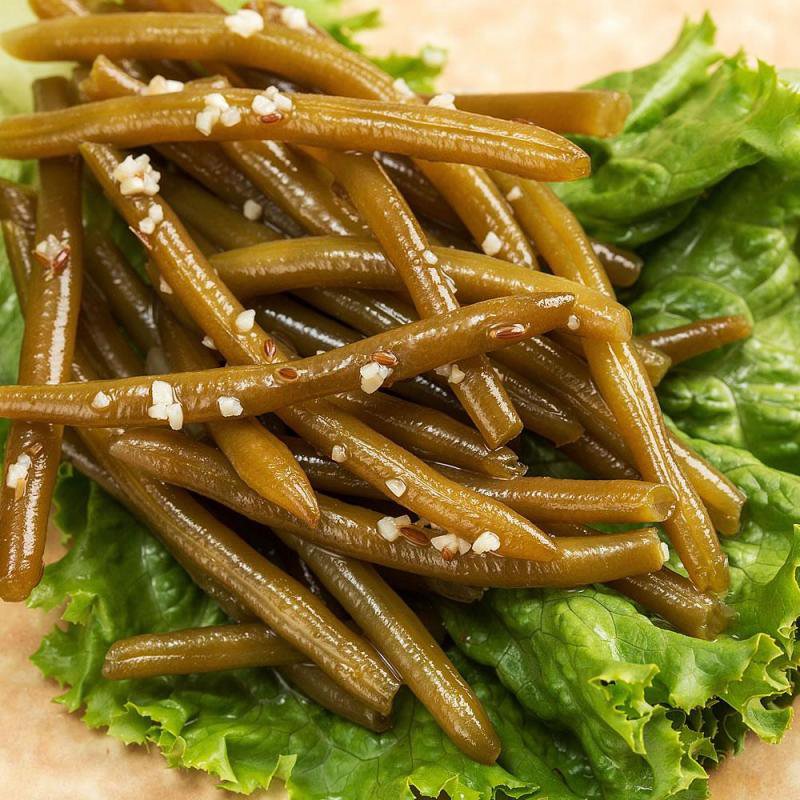 Close-up of handpicked pickled dilly beans sprinkled with garlic and spices, served on fresh green leafy lettuce, highlighting a unique Amish-made USA product in Kitchen & Food collections.