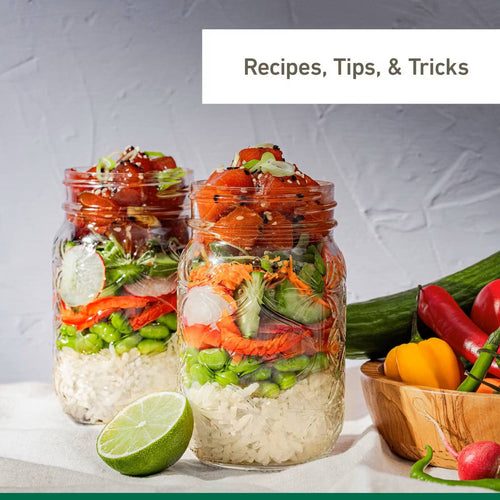 Two clear jars layered with fresh vegetables and rice, shown with a halved lime and colorful peppers nearby, promoting homemade recipes and food preservation ideas.