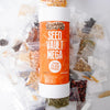 Tall white and orange container labeled for storing a large variety of heirloom seeds, surrounded by small clear plastic packets of assorted seeds, ideal for Farm, Garden & Tool and Seeds and Planting collections.