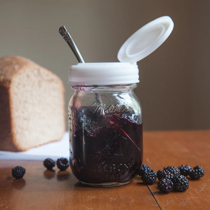 Clear glass jar filled with blackberry jam topped with a white flip top lid open to reveal a spoon inside, handcrafted and made in USA, ideal for Kitchen Gadgets, Storage and Serving, Home & Decor, and Best Sellers collections.