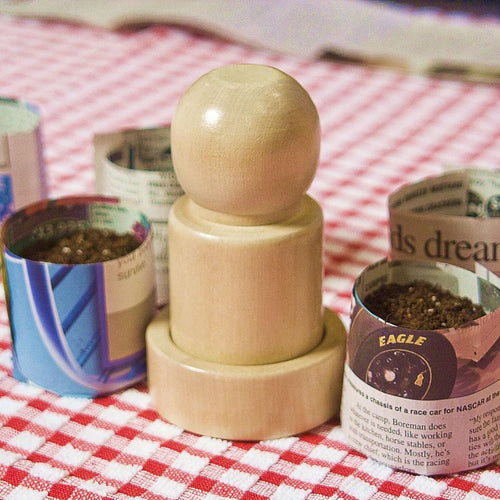 Handcrafted wooden pot maker tool used to form newspaper seedling pots, surrounded by recycled newspaper pots filled with soil, ideal for Farm, Garden & Tool, Garden Accessories, Seeds and Planting, Best Sellers, and Promo Eligible collections.