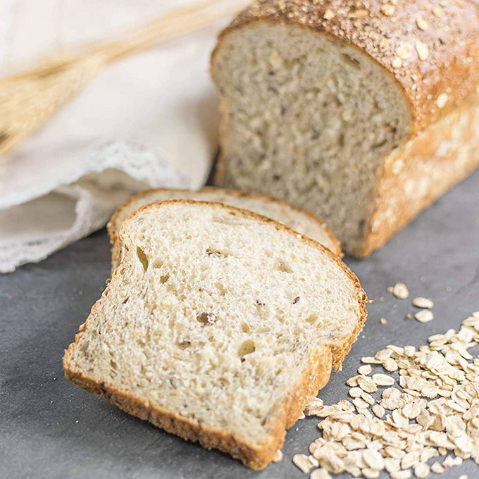 Two slices of homemade oat bread with a soft crumb, resting on a grey surface next to raw oats, styled for Kitchen & Food, Baking Supplies, and Bread Making collections.