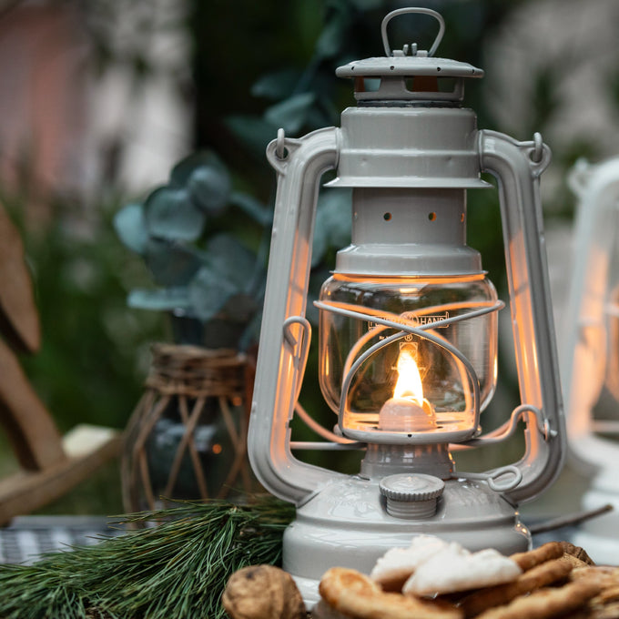 Handcrafted galvanized oil lantern with thermal heat-resistant globe glowing warmly outdoors on a rustic table with pine branches and natural decor, ideal for Lamps & Lighting, Camping, and Emergency Supplies collections.