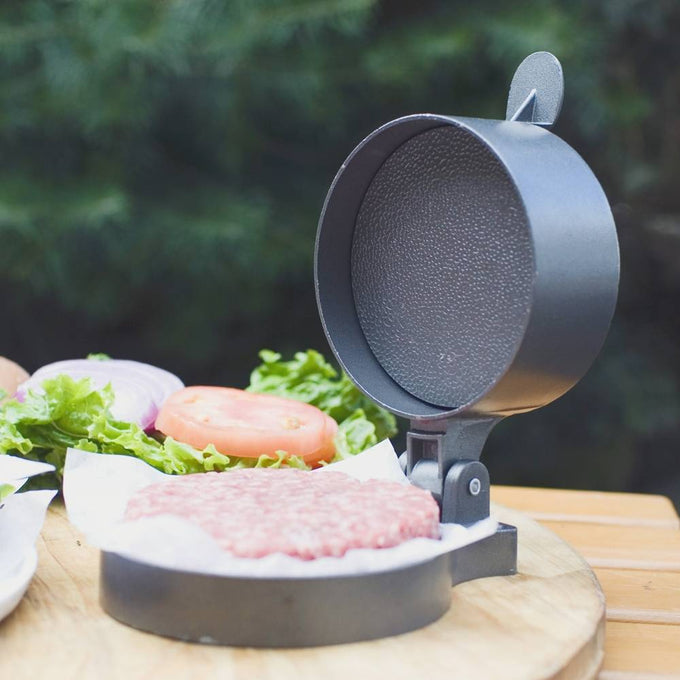 Heavy-duty metal patty press with textured pressing surface and hinge lid, used for shaping uniform hamburger patties, featured in Kitchen & Food and Specialty Equipment collections.