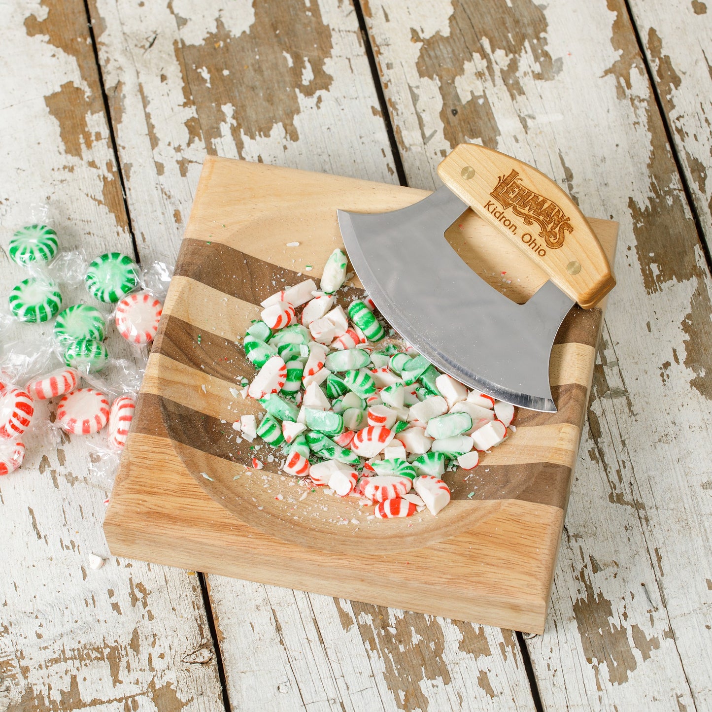 Handcrafted ulu knife with crescent-shaped stainless steel blade and engraved wooden handle resting on a striped wooden chopping bowl with crushed red and green peppermint candies, ideal for food prep in Kitchen & Food, Knives & Axes, and Kitchen Accessories collections.
