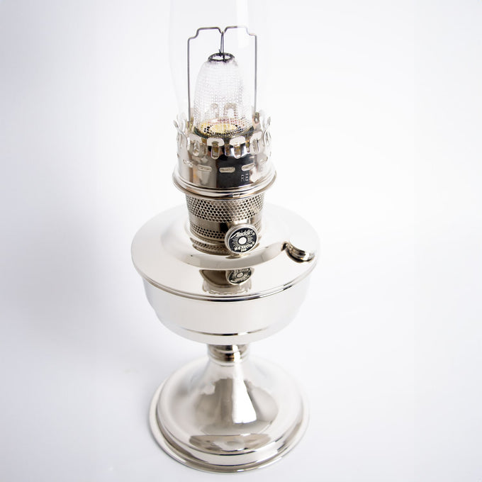 Polished chrome oil lamp with a bright wick and glass chimney, handcrafted and designed for lamps and lighting, oil lamp, and table lamp collections.