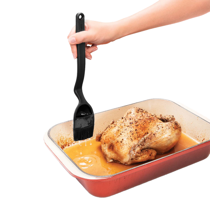 Black basting brush with ergonomic handle and flexible head designed for controlled liquid release over roasted chicken in a baking dish, ideal for Kitchen & Food and Grilling collections.
