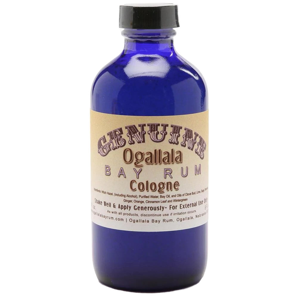 Blue glass bottle of handcrafted cologne made in USA with vintage-style beige label for health and wellness and grooming collections, featuring a manly bay rum scent.