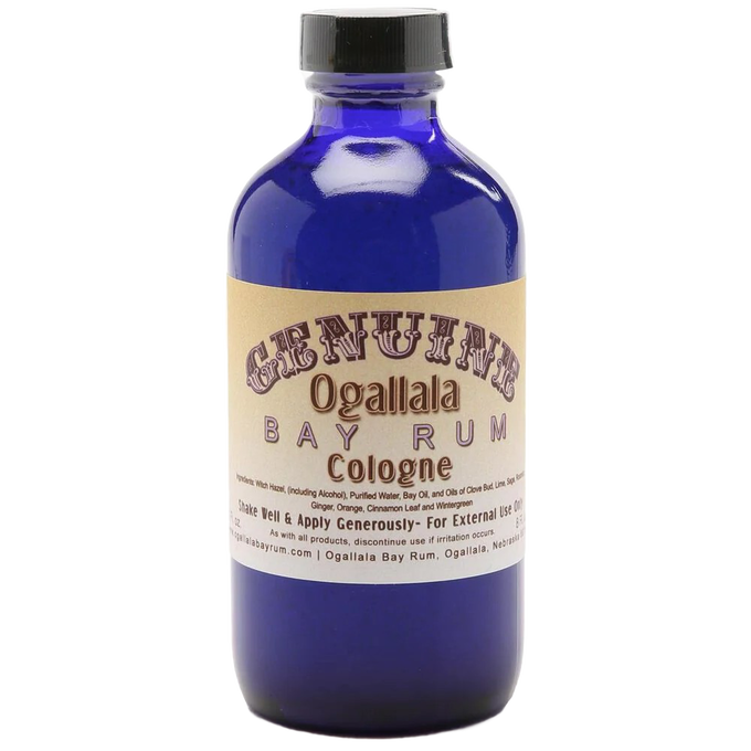 Blue glass bottle of handcrafted cologne made in USA with vintage-style beige label for health and wellness and grooming collections, featuring a manly bay rum scent.