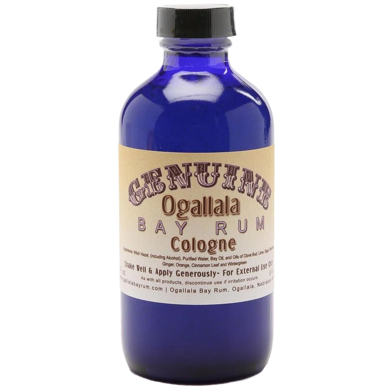 Blue glass bottle of handcrafted cologne made in USA with vintage-style beige label for health and wellness and grooming collections, featuring a manly bay rum scent.