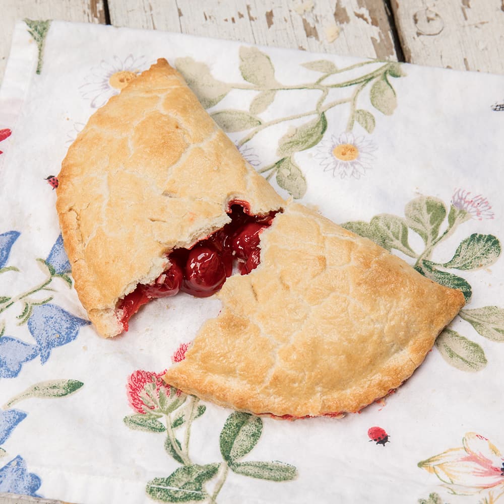 Generously filled fruit turnover with a golden, flaky crust broken open to reveal bright red fruit filling, highlighting a handcrafted treat from USA Made and Kitchen & Food collections.