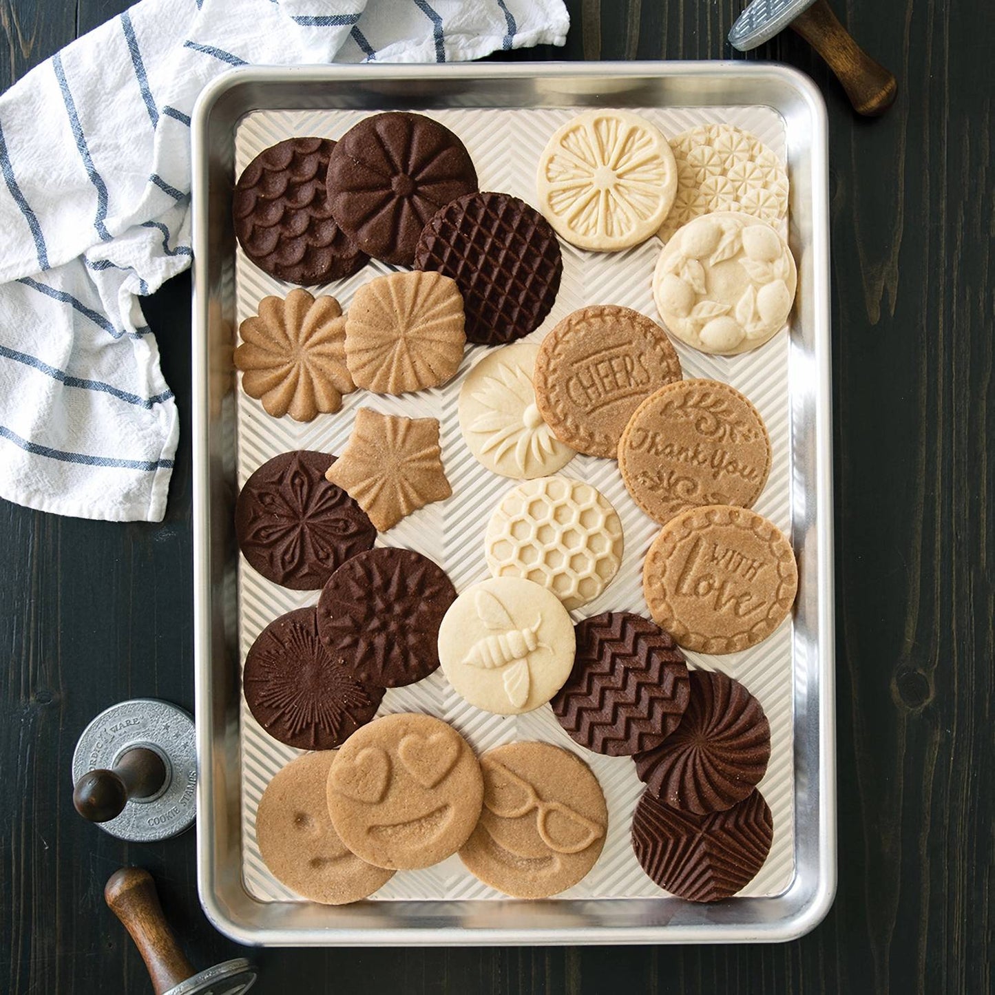 Half-sheet aluminum baking pan with prism grid holding an assortment of intricately patterned cookies, showcased with kitchen tools for baking and food preparation collections.