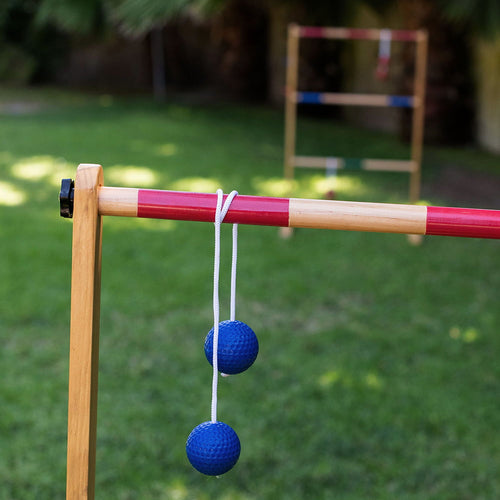 Handcrafted wooden double ladder frame with red and natural finish, featuring two blue golf ball bolas suspended by white cords, set outdoors in lawn games, best sellers, promo eligible collections.