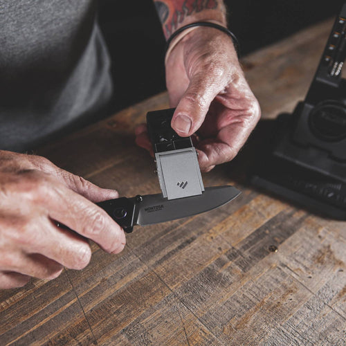 Person using an adjustable angle knife sharpener with a black folding knife on a rustic wooden surface, suitable for Farm, Garden & Tool and Kitchen & Food collections.
