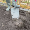 Close-up of a heavy-duty digging spade with forged carbon steel head cutting into rich garden soil, held by a person wearing gray gardening boots, ideal for Farm, Garden & Tool, Digging and Cultivating, Lawncare, Best Sellers, and Promo Eligible collections.