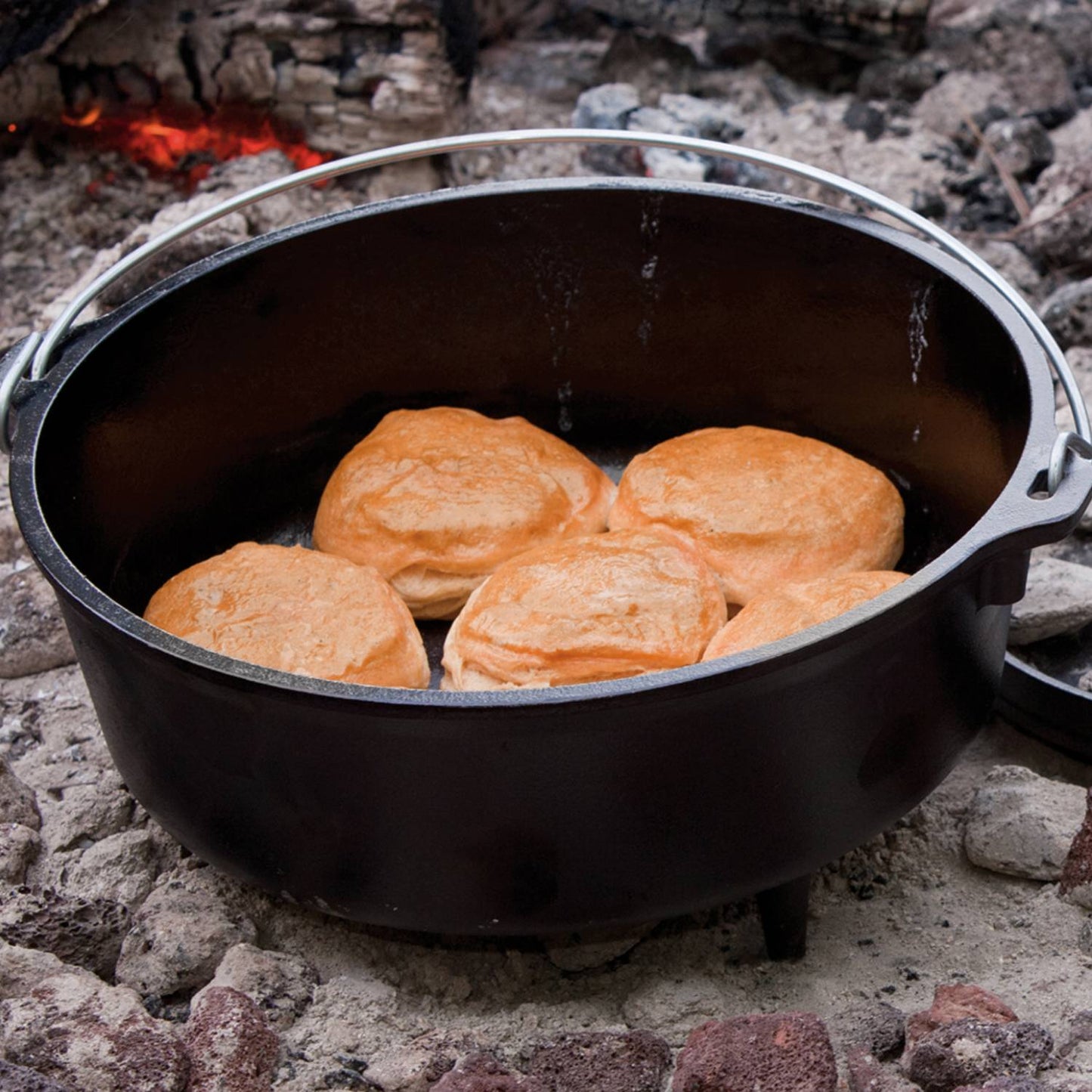 Handcrafted cast iron camp Dutch oven with built-in legs baking golden biscuits over hot coals outdoors, featured in Farm, Garden & Tool, Camping, Cast Iron, USA Made, Best Sellers, Promo Eligible collections.