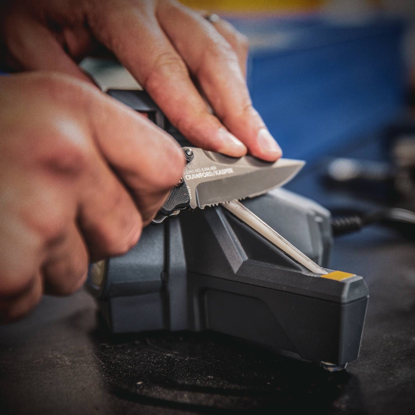 Close-up of hands sharpening a serrated knife with a compact powered abrasive belt sharpener combined with a manual ceramic honing rod, ideal for Farm, Kitchen, and Tool collections.