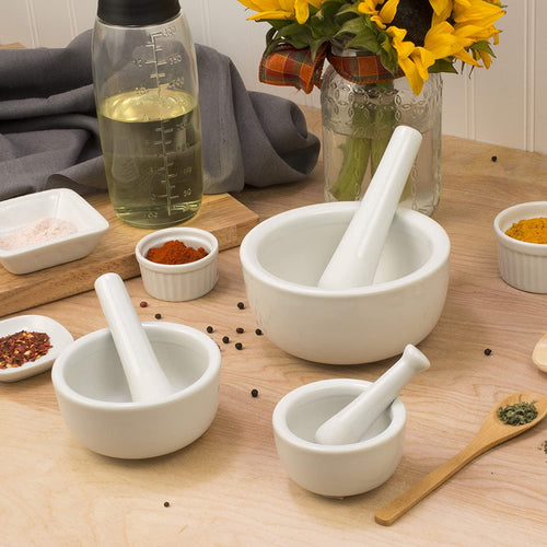 Set of three white porcelain mortar and pestles in small, medium, and large sizes, arranged on wooden surface with spices and oil, ideal for efficient food preparation in Kitchen & Food collections.