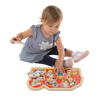 Toddler sitting and playing with a handcrafted wooden farm animal puzzle featuring jumbo knobs on a bright red barn background, encouraging fine motor skills development in children.