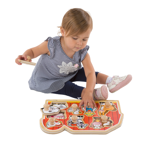 Toddler sitting and playing with a handcrafted wooden farm animal puzzle featuring jumbo knobs on a bright red barn background, encouraging fine motor skills development in children.
