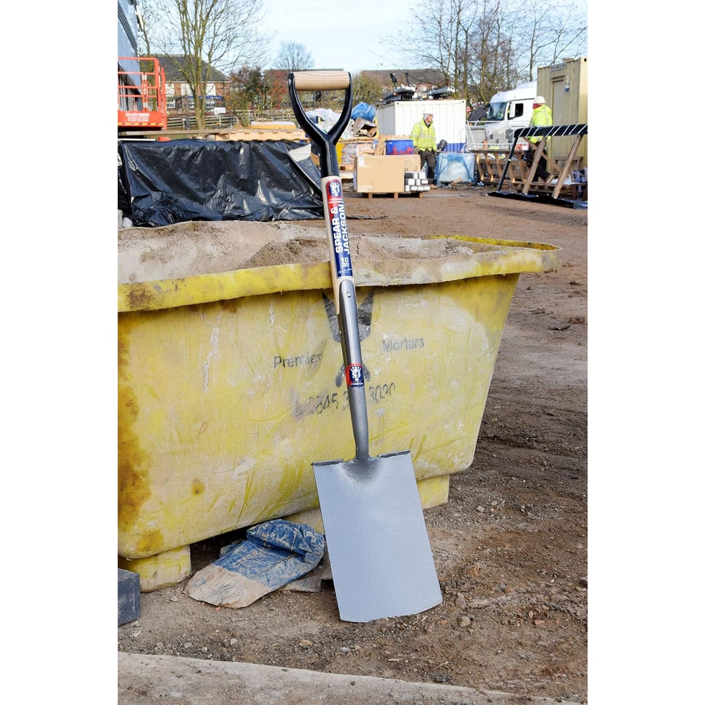 Heavy-duty spade with forged carbon steel blade and D-shaped wooden handle standing upright against a yellow construction skip, perfect for Farm, Garden & Tool, Digging and Cultivating, Lawncare, Best Sellers, and Promo Eligible collections.