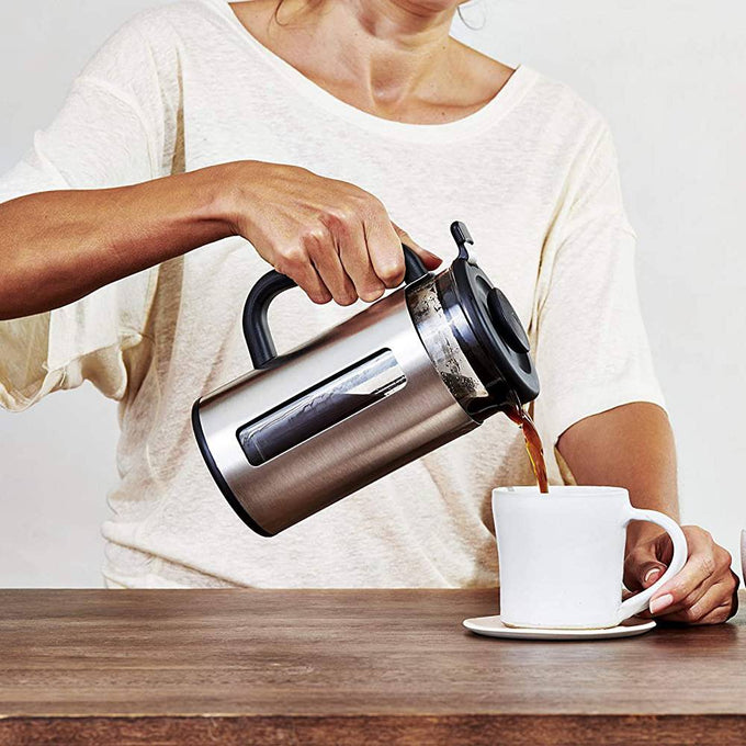 Person pouring coffee from a stainless steel French press with black handle into a white ceramic cup on a wooden table, featured in Kitchen & Food, Brewing Coffee and Tea collections.