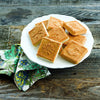 Plate of golden square shortbread cookies with decorative patterns on top, set on rustic wooden surface with floral patterned cloth, matching Kitchen & Food collections.