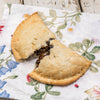 Golden-brown handcrafted fruit turnover with flaky crust and rich, dark filling, resting on a floral-patterned cloth, featured in Kitchen & Food, Snacks and Sweets, and USA Made collections.