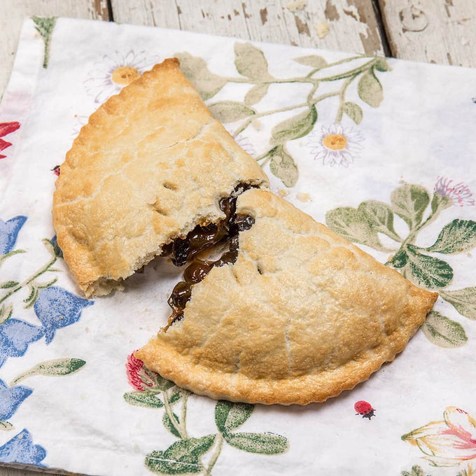 Golden-brown handcrafted fruit turnover with flaky crust and rich, dark filling, resting on a floral-patterned cloth, featured in Kitchen & Food, Snacks and Sweets, and USA Made collections.