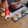 Handcrafted FinaMill grinder in vibrant red being used to season a dish with mixed spices, shown alongside interchangeable pods filled with various whole spices on a kitchen countertop, ideal for Kitchen & Food, Kitchen Gadgets, Kitchen Accessories, Best Sellers, and Promo Eligible collections.