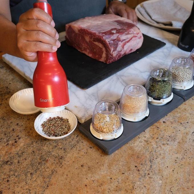 Handcrafted FinaMill grinder in vibrant red being used to season a dish with mixed spices, shown alongside interchangeable pods filled with various whole spices on a kitchen countertop, ideal for Kitchen & Food, Kitchen Gadgets, Kitchen Accessories, Best Sellers, and Promo Eligible collections.