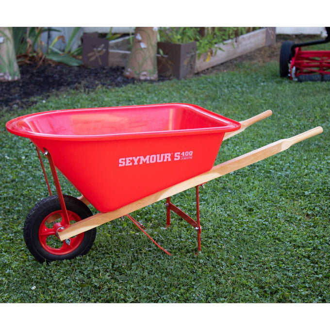 Bright red child's wheelbarrow with solid wooden handles, a durable metal frame, and rubber tire, displayed outdoors on grass, suitable for lawn games and toys collections.