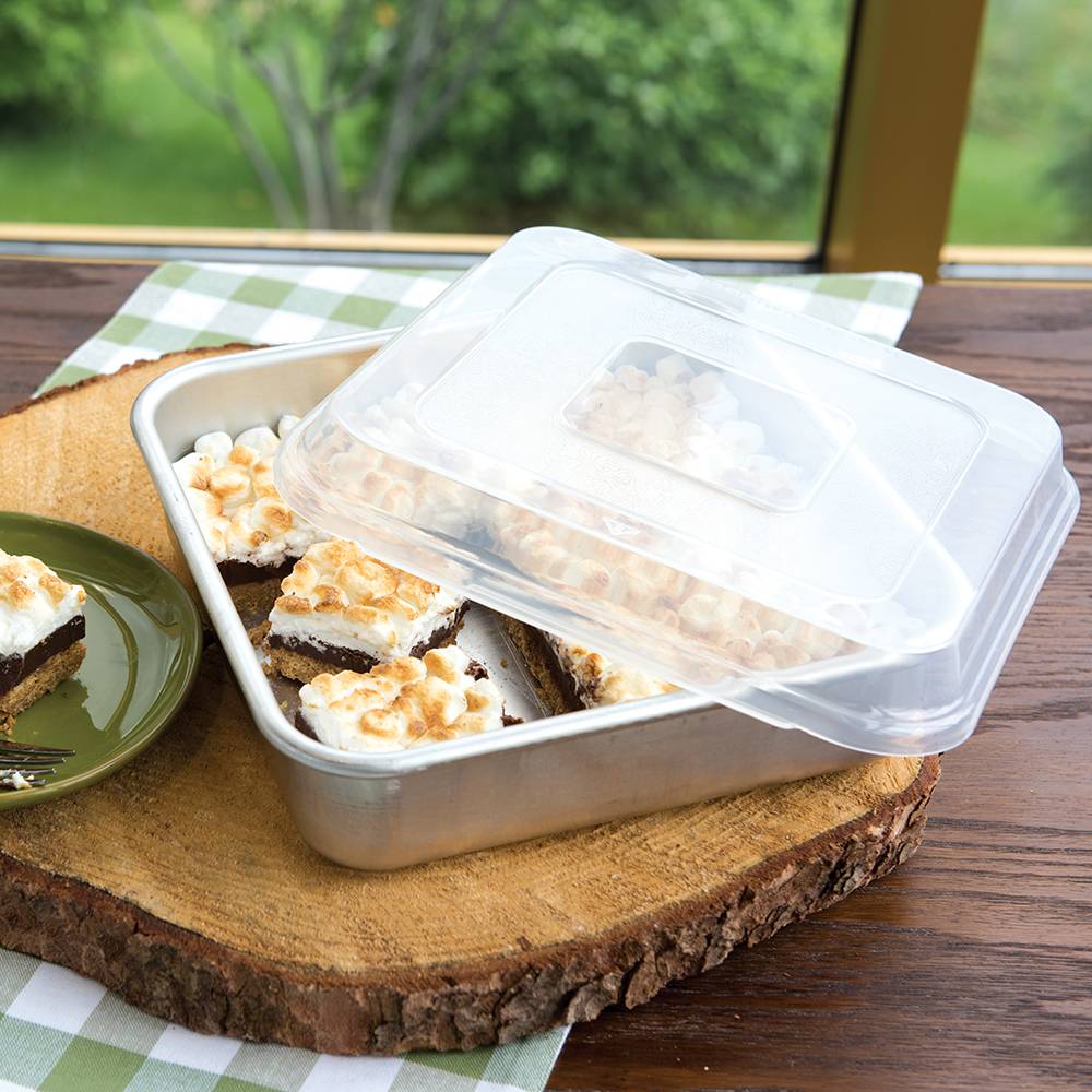 Square aluminum cake pan with encapsulated galvanized steel rim and clear plastic lid, holding toasted marshmallow dessert bars on a wooden slab, perfect for kitchen and baking supplies.