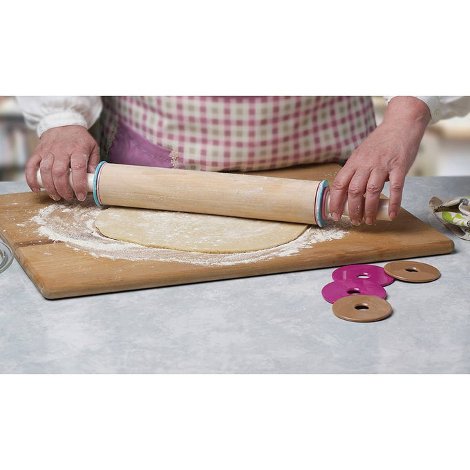 Hands using a beechwood adjustable rolling pin with removable discs to roll out dough on a floured wooden board, part of kitchen and baking supplies collections.